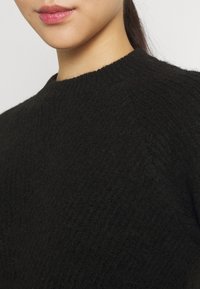 Suéter de punto negro con cuello redondo, que presenta un patrón texturizado y detalles acanalados en el cuello para mayor estructura.