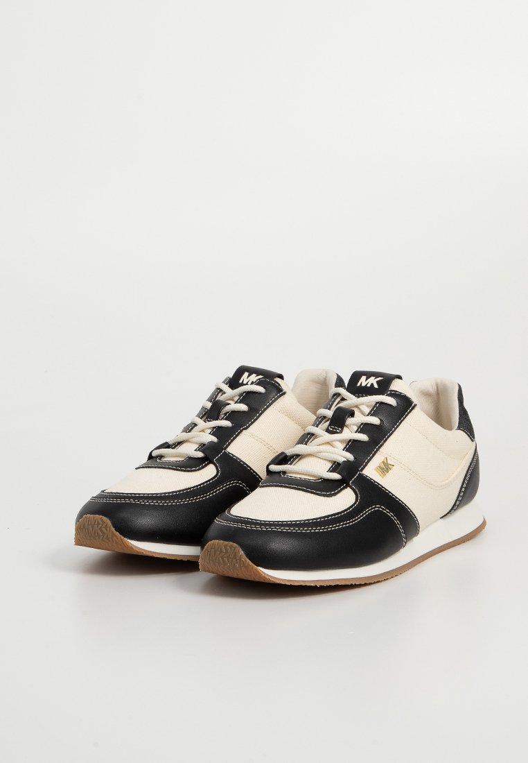 Svarta och krämfärgade träningsskor som har material av kanvas och läder, rund tå, vit sula, texturerad gummiyttersula och dekorativ sömnad.