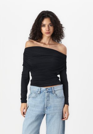 Black off-the-shoulder top with ruched texture, long sleeves, and a slim fit, worn with high-waisted light blue jeans.