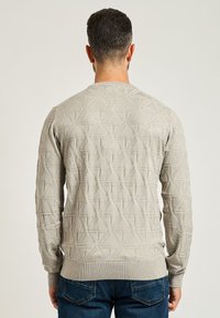 Maglione lavorato a maglia grigio chiaro con un motivo geometrico testurizzato, scollatura tonda e polsini e orlo a coste. Indossato con jeans in denim blu.