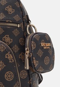 Sac à dos Guess noir et marron à motif avec des fermetures éclair dorées et une petite pochette attachée avec le logo Guess et une tirette.