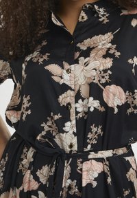 Sort blomsterkjole med knapdetaljer, der har lyserøde og beige blomster mønstre. Letvægtsstof med belted talje og korte ærmer.