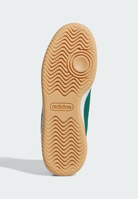 Adidas sneakersåls utsida har ett vågigt mönster, ett ljusbrunt gummimaterial och en cirkulär insats med präglad logotyp.