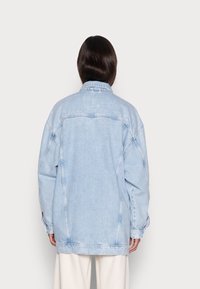 Ljusblå denimjacka med oversized passform, minimalistisk sömnad, klassisk krage och lång ärm, med rak skärning och sidofickor.