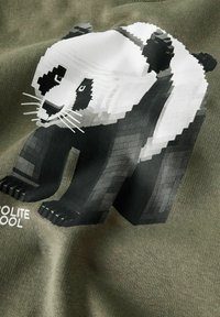 Zielona tkanina z pikselowym czarno-białym wizerunkiem pandy. Pod pandą znajduje się napis "POLITE COOL". Miękka faktura z casualowym wzorem.