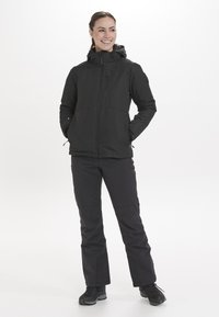 Schwarze isolierte Jacke mit Kapuze und Frontreißverschluss, kombiniert mit schwarzen Hosen. Merkmale sind seitliche Taschen und ein schlankes, aerodynamisches Design.
