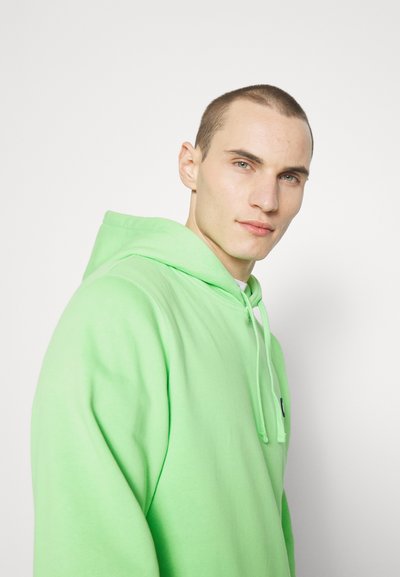 Lys grønn hettegenser med snorhette, myk tekstur og en liten kontrastlogo foran. Har en avslappet passform.