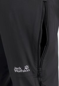 Zwarte lichtgewicht broek met een zijzak met ritssluiting, met een gladde textuur en een in het grijs gedrukt logo, geplaatst nabij de heup.