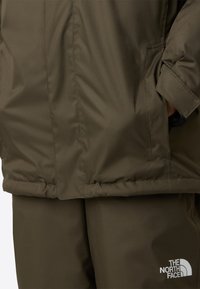 Vanntett jakke i olivengrønn med glatt tekstur, utstyrt med høy krage, elastiske mansjetter og en logo på kanten.