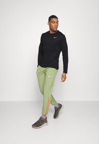 Czarna koszulka Nike z długim rękawem, jasnoszare zwężane spodnie z pomarańczowymi paskami po bokach i szare trampki z pomarańczowymi akcentami, noszone przez modela.