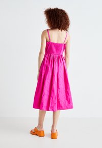 Rochie din bumbac roz, cu un corset plisat, bretele ajustabile și o fustă evazată. Asortată cu sandale cu toc chunky, de culoare portocalie.