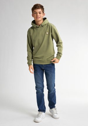Grüne Kapuzenpullover mit Kordelzug und kleinem Logo-Patch, kombiniert mit blauen Jeans und weißen Turnschuhen auf einem hellen Hintergrund.