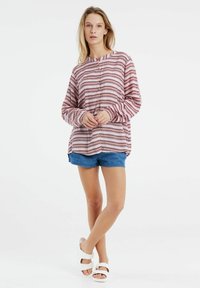 Pullover a righe in tonalità di rosa e bordeaux con una vestibilità rilassata, maniche lunghe e scollatura rotonda, abbinato a pantaloni di jeans a shorts.