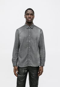 Grå skjorta med knappknäppning och texturerat tyg, med klassisk krage och långa ärmar, kombinerad med svarta cargobyxor i läder.