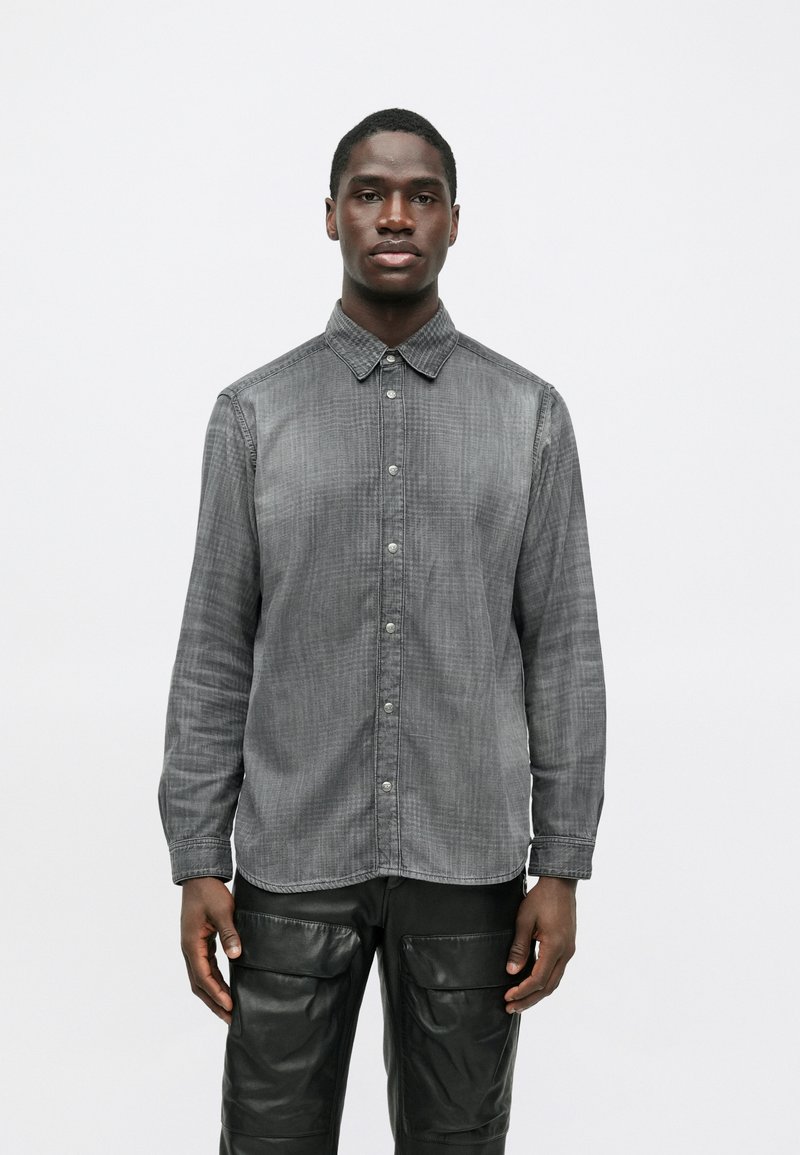 Grå skjorta med knappknäppning och texturerat tyg, med klassisk krage och långa ärmar, kombinerad med svarta cargobyxor i läder.