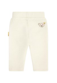 Cremfarbene, gestrickte Babyhosen mit einem elastischen Bund und einem kleinen gestickten Bärenmotiv am linken Bein. Glatte Texture.