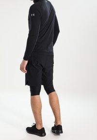 Svart långärmad träningsskjorta, åtsittande design, kombinerad med svarta shorts och tajta leggings. Svarta sneakers fulländar outfiten.