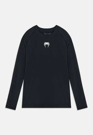 Chemise noire à manches longues avec un petit logo blanc représentant un visage d'animal stylisé avec des crocs, centré sous l'encolure.