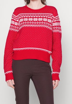 Red knitted sweater with white snowflake and heart patterns, worn with dark brown pants, shown from neck to hips.