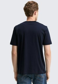 Granatowa koszulka z krótkim rękawem wykonana z miękkiego materiału, z okrągłym dekoltem i prostym wykończeniem, noszona z niebieskimi dżinsami.