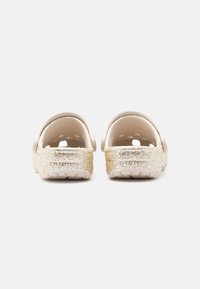 Λαμπερά χρυσά παπούτσια slip-on με λείο λευκό επάνω μέρος και υφή στρωμένη με γκλίτερ στη σόλα, με στρογγυλεμένες πλάτες και κοντούς πλαϊνούς τοίχους.