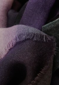 Geweven sjaal in gradiënttinten van paars en donkergroen, met een zachte textuur en franjes aan de randen. Zichtbare patronen in de stofweving.