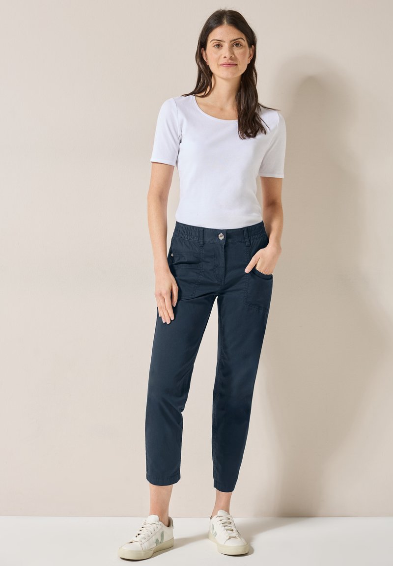 Pantalons cropped légers bleu marine avec taille élastique et poches avant, associés à un t-shirt blanc ajusté à manches courtes et des baskets blanches.