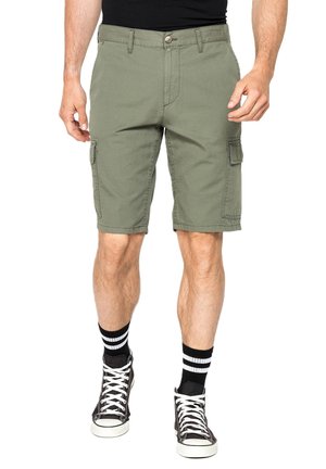 Uomo con pantaloncini cargo verde oliva, calzini a righe bianche e nere e sneakers alte nere, in piedi su sfondo bianco.
