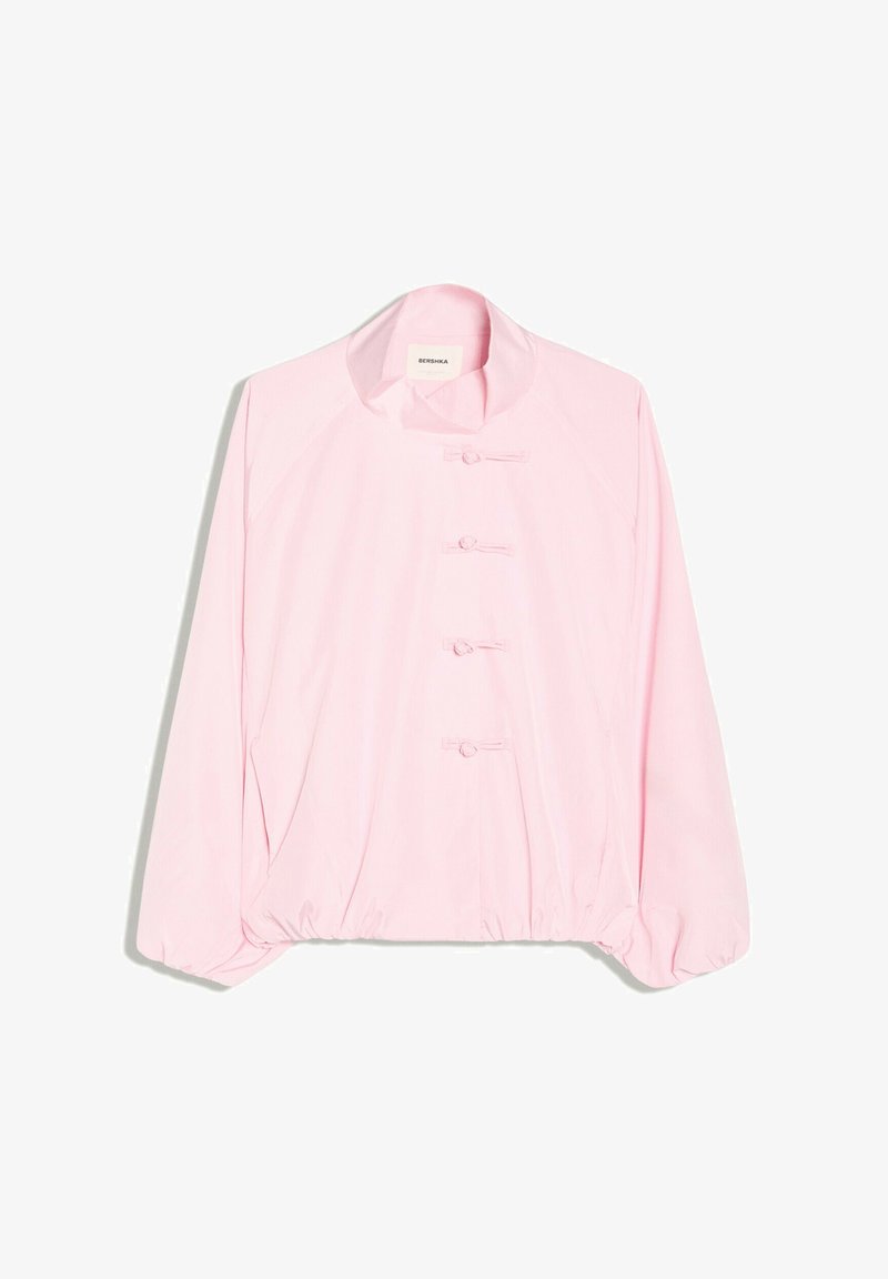 Veste rose clair à manches longues avec un col montant et quatre fermetures à boutons noués en tissu sur le devant.