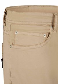 Beige katoenen broek met een gedeeltelijk zichtbaar achterzak met zilveren hardware en gestikt detail. Zachte textuur en klassiek ontwerp.