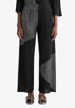 Pantaloni neri a gamba larga con pieghe verticali e grandi toppe diagonali argentate glitterate, indossati con scarpe Mary Jane metallizzate.
