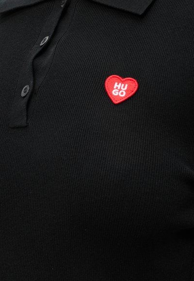 Polo noir côtelé avec trois boutons et un petit patch en forme de cœur rouge brodé "HUGO" sur la poitrine gauche.