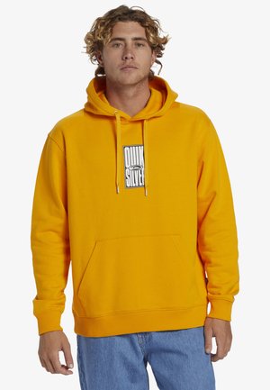 Yellow hooded sweatshirt with a front kangaroo pocket, featuring a black and white logo patch. Soft fabric texture and ribbed cuffs.