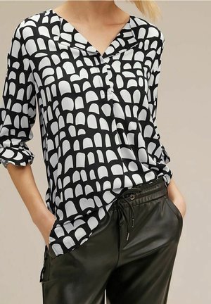 Zwart-witte blouse met een geometrisch boogpatroon, v-hals, 3/4 mouwen en een ontspannen pasvorm, gecombineerd met zwarte neplederen broeken.