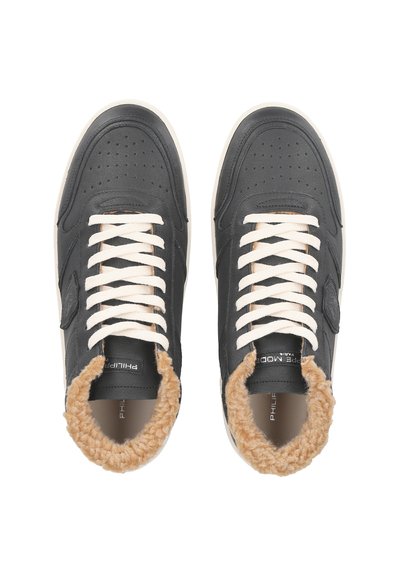 Black leather sneakers with cream laces, featuring a fluffy tan collar and perforated design on the toe area. Rubber sole.
