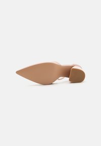 Nude high-heeled shoe with a pointed toe, smooth finish, and a chunky heel. The sole features a textured pattern for grip.