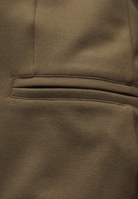 Κοντινή λήψη ενός καφέ ρούχου από ύφασμα με οριζόντια τσέπη με σχισμή και λεπτομερείς ραφές.