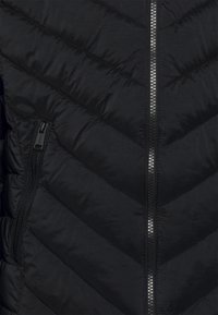 Giacca nera imbottita con motivo a zigzag, dotata di una cerniera centrale metallica e di una tasca laterale con zip. Texture liscia e design leggero.