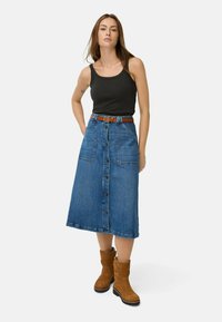 Denim A-line nederdel med frontknapper og to store lommer, parret med en sort tanktop og brune ruskind ankelstøvler.