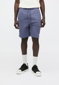 Lilla bomuldsblandede shorts med elastisk talje og snøre, med sidelommer og løs pasform, kombineret med hvide sokker og sorte sneakers.