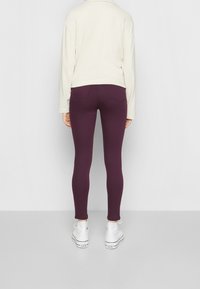 Leggings burdeos hechos de una tela elástica, con un ajuste ceñido y un diseño minimalista. Combinados con una blusa ligera y suelta y zapatillas blancas.