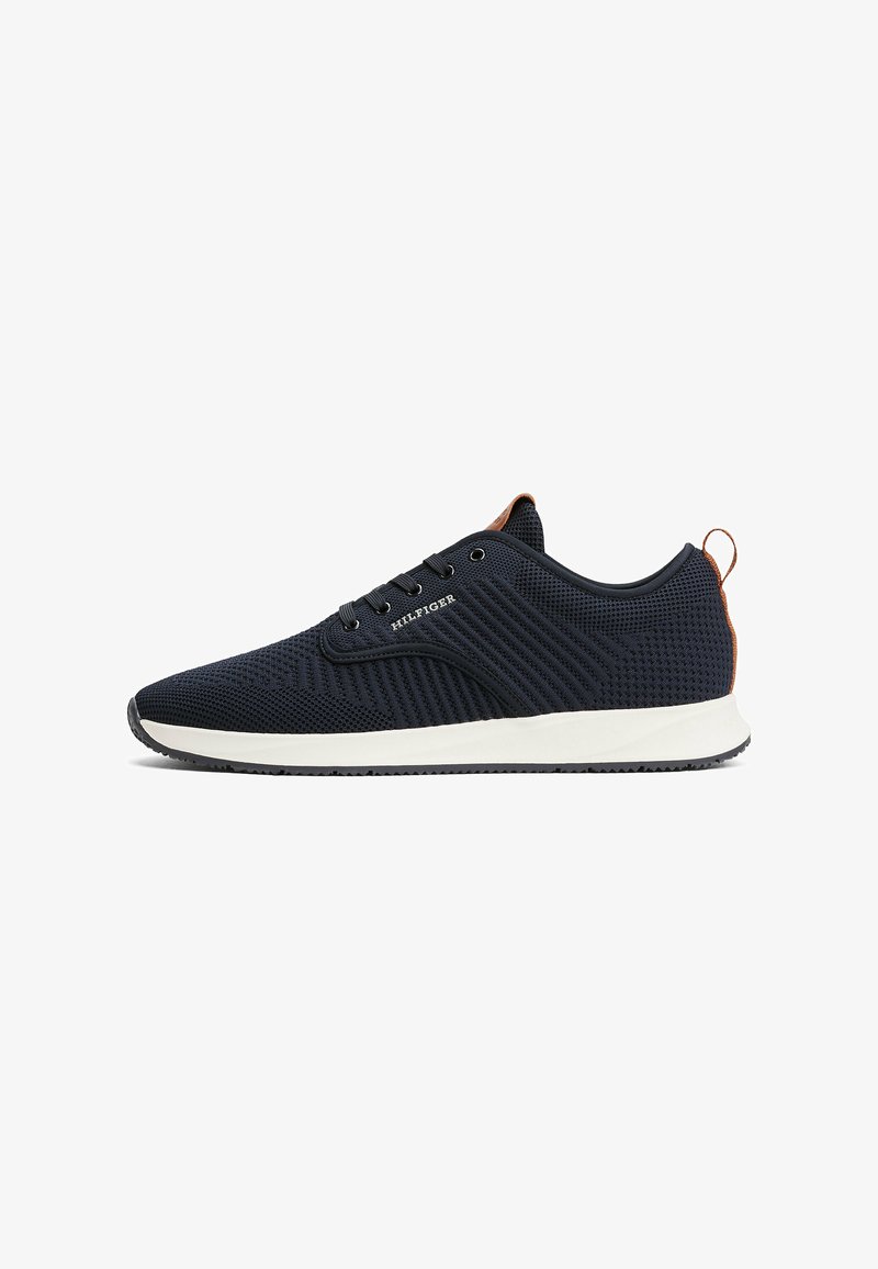 Zapatilla de malla azul marino con suela blanca, diseño texturizado, ojales de metal y acento marrón en el talón. Estilo minimalista con cordones.