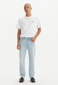 Camiseta blanca de algodón con el logo negro de "Levi's", combinada con unos jeans rectos de mezclilla azul claro y mocasines negros. Diseño sencillo y ajuste relajado.