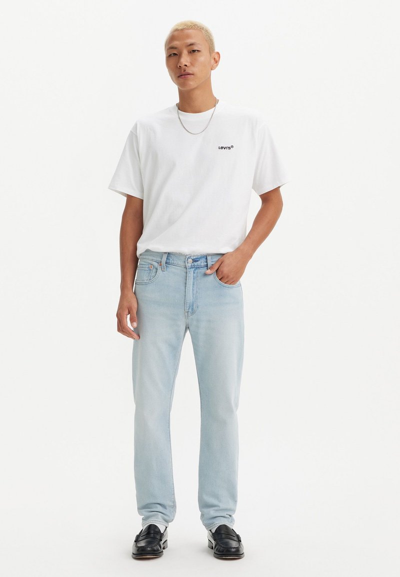Bijela pamučna majica s crnim "Levi's" logom, uparen s svijetloplavim ravnim trapericama i crnim mokasinkama. Jednostavan dizajn i opušten kroj.