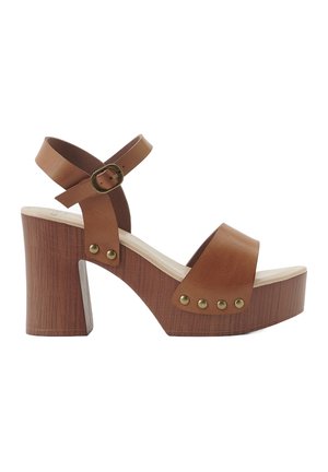 Sandali platform in pelle marrone con cinturino alla caviglia, tacco in legno chunky e borchie metalliche lungo il midsole. Texture liscia e design con punta aperta.