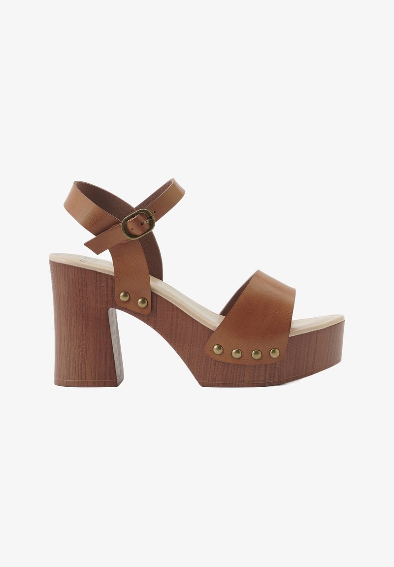 Sandali platform in pelle marrone con cinturino alla caviglia, tacco in legno chunky e borchie metalliche lungo il midsole. Texture liscia e design con punta aperta.