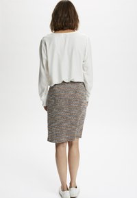 Blouse blanche à manches longues avec manches bouffantes, associée à une jupe crayon texturée à motif multicolore, et des baskets blanches.