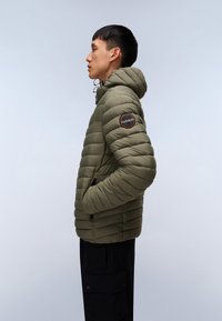 Giubbotto imbottito verde oliva con cappuccio, caratterizzato da un design trapuntato orizzontale, tasche laterali e un'etichetta rotonda con logo sulla manica sinistra.