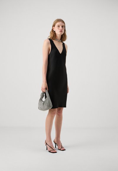 Robe noire à bretelles avec un décolleté en V. Accompagnée d'un sac à main texturé gris et de sandales à talons noires. Finition en tissu lisse.