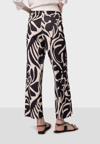 Pantalons fluides noirs et crème présentant un grand motif abstrait, fabriqués à partir d'un tissu doux avec une texture légèrement brillante, et une coupe ample.